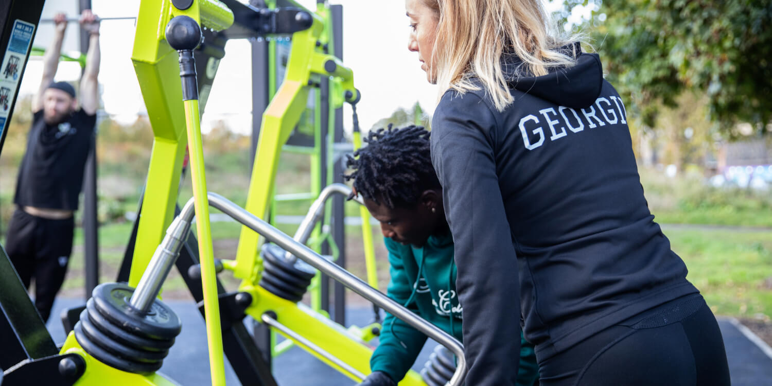 A trainer supervises as an individual adjusts a fitness machine designed for strength training.